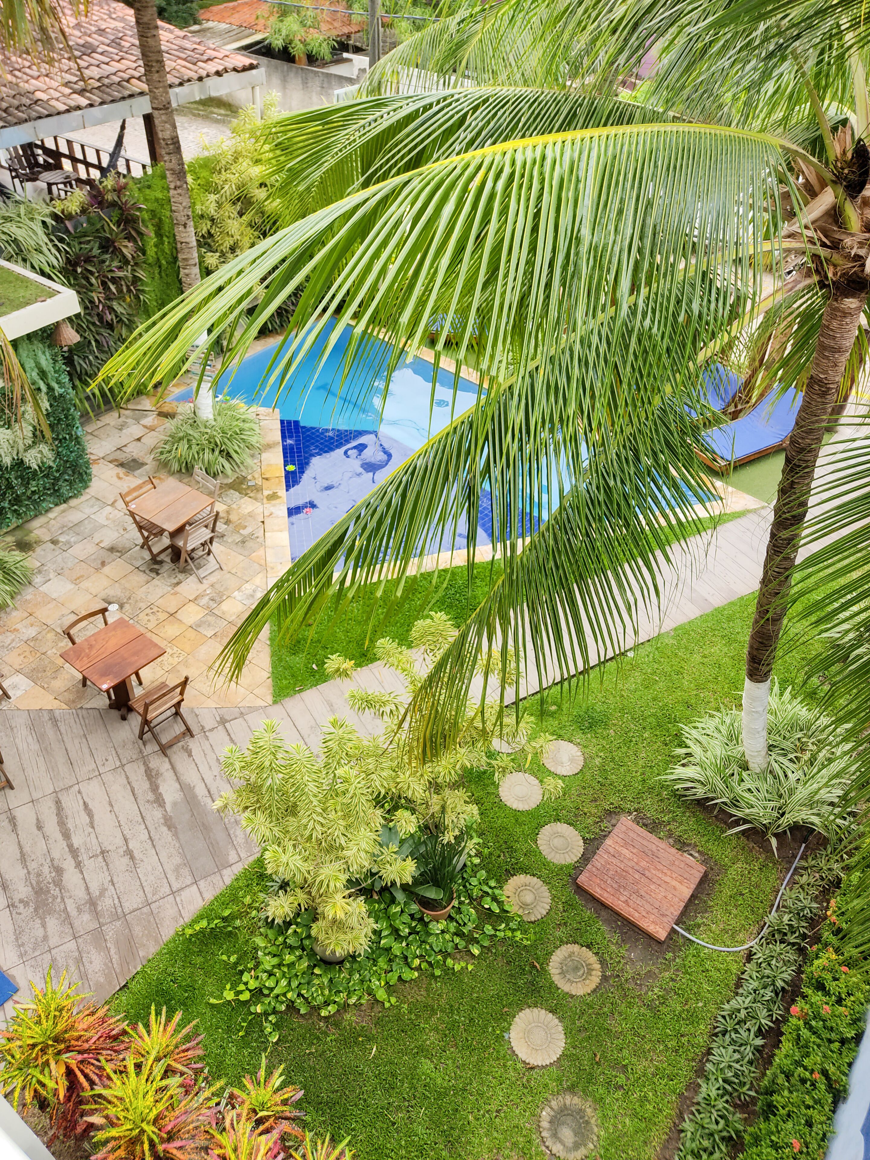 A pool area with a wooden deck, a table and chairs, and various plants.