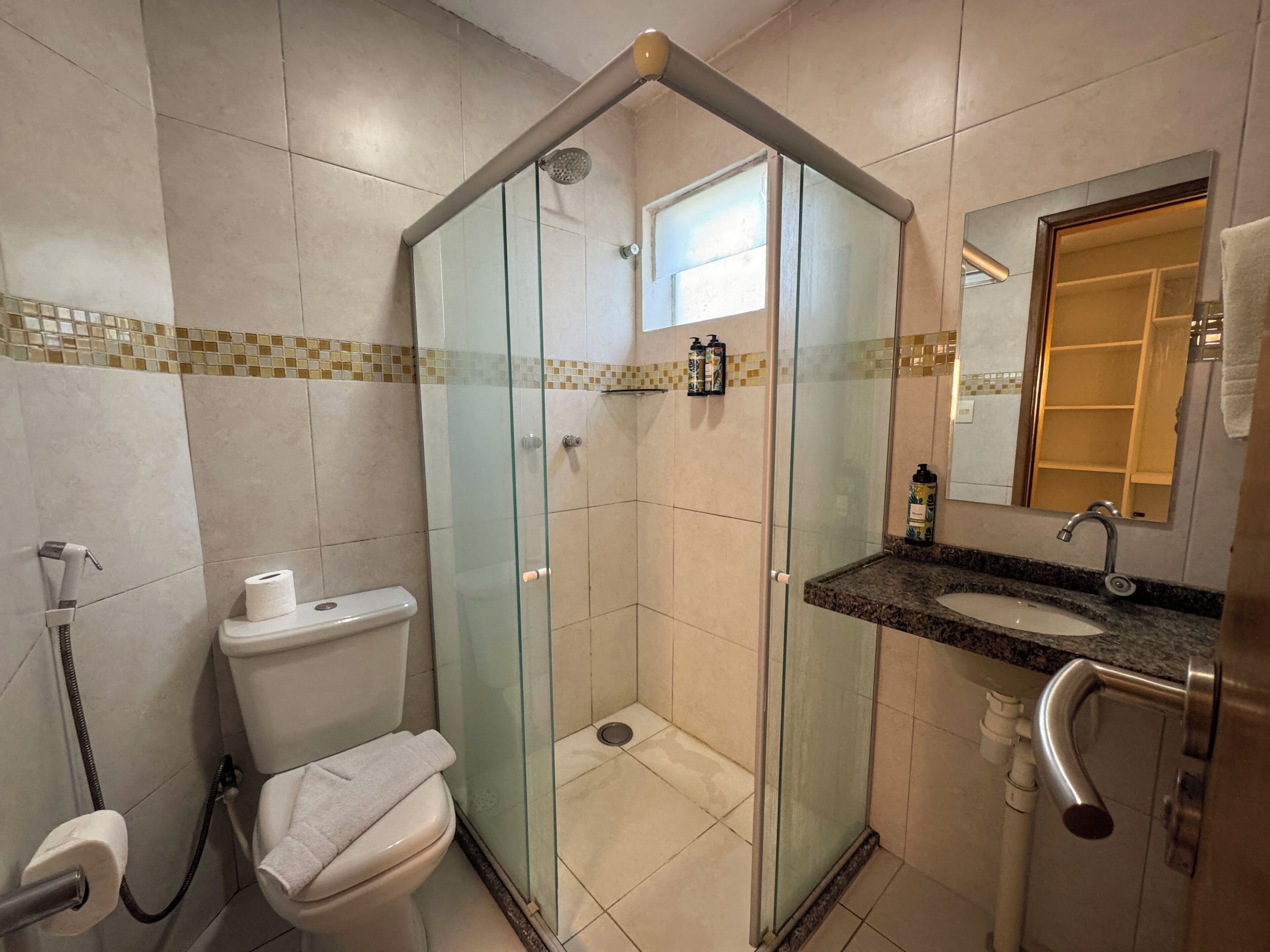 Ein Badezimmer mit Duschkabine, Toilette, Waschbecken mit Spiegel und Handtuchhalter.