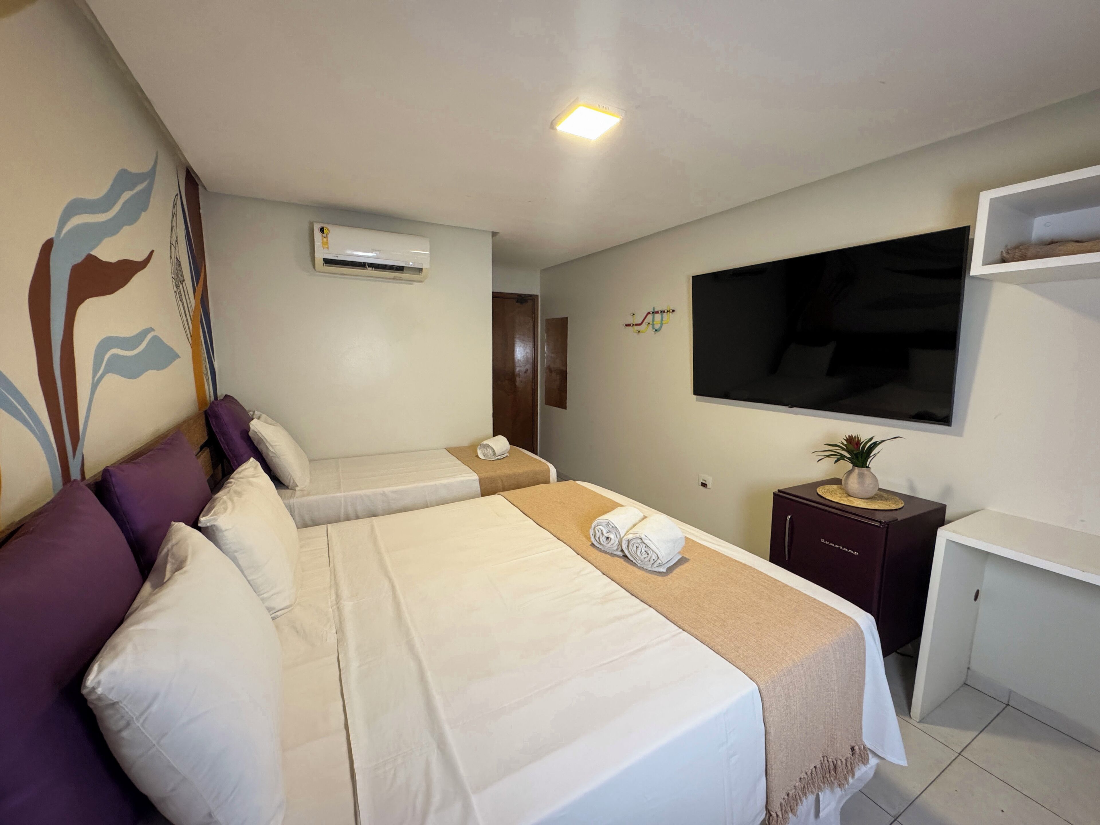 A hotel room with two beds, a TV, a small desk, and an air conditioning unit.