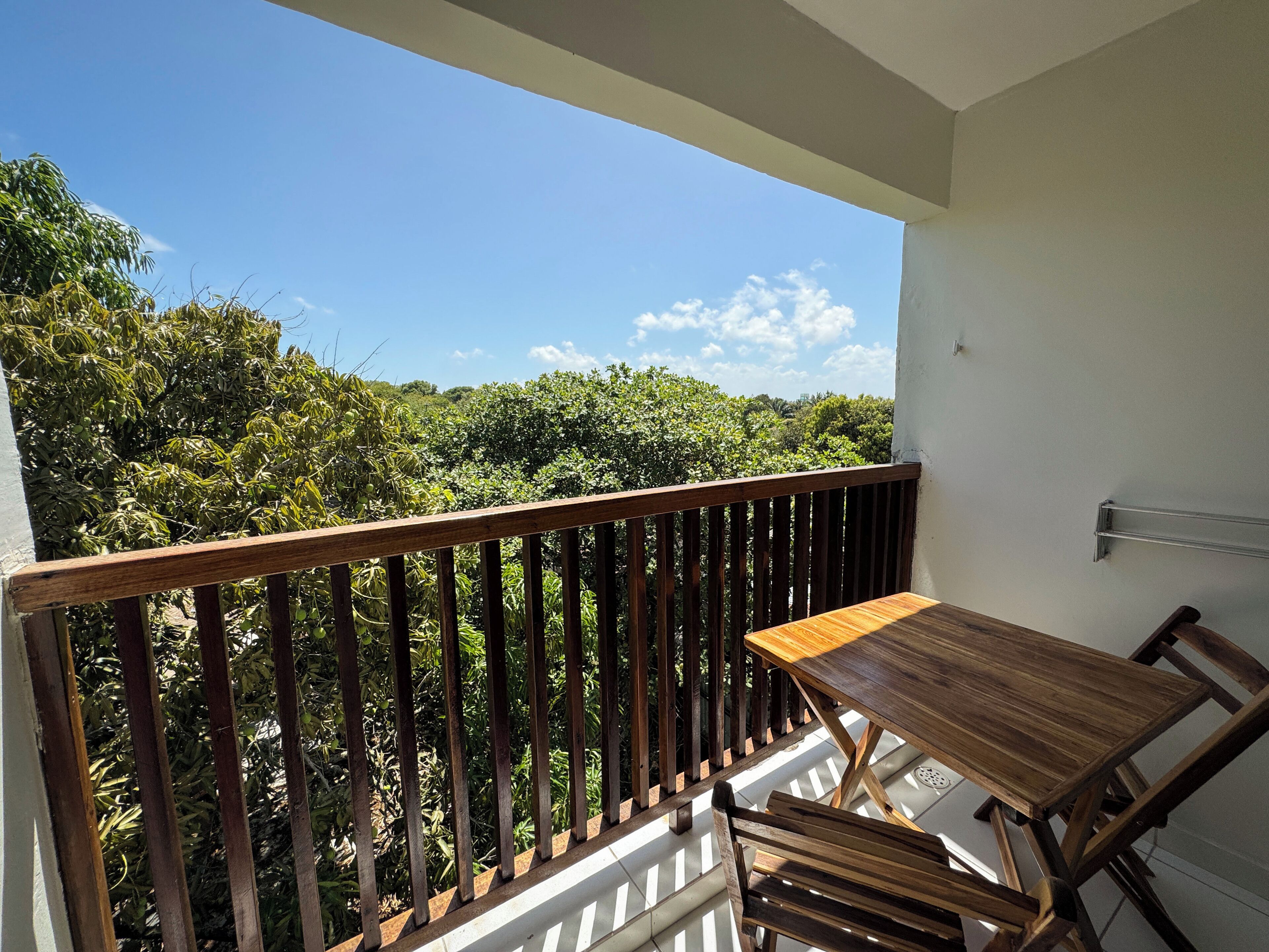 A balcony with a wooden table and chairs, overlooking a lush green landscape.