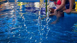 A swimming pool with clear water, surrounded by palm trees and a white building in the background. - Pousada Unaí (Ipojuca)