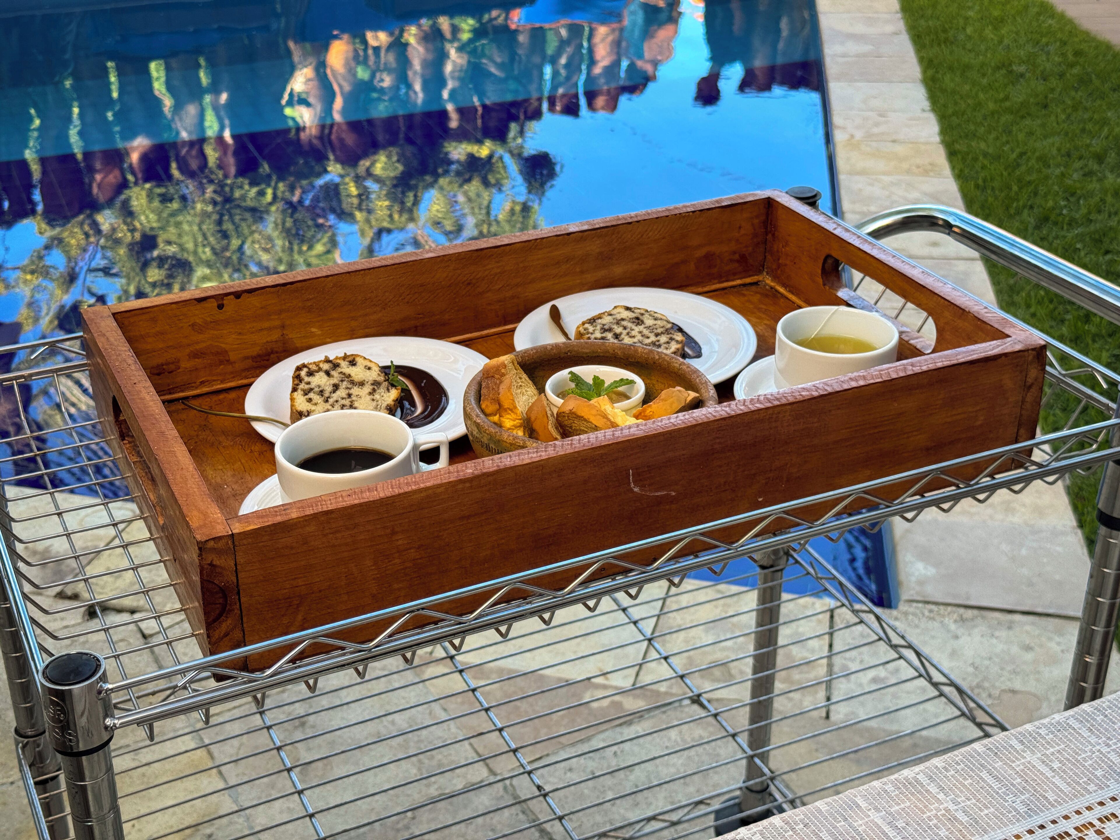 Un vassoio di legno con cibo e bevande su un carrello metallico vicino a una piscina.