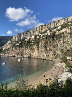 A coastal town with buildings on a cliff overlooking the sea, a sandy beach, and boats in the water.