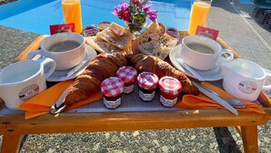 Un plateau de petit-déjeuner avec des croissants, des pâtisseries et des confitures, posé sur un balcon donnant sur une piscine et la mer.