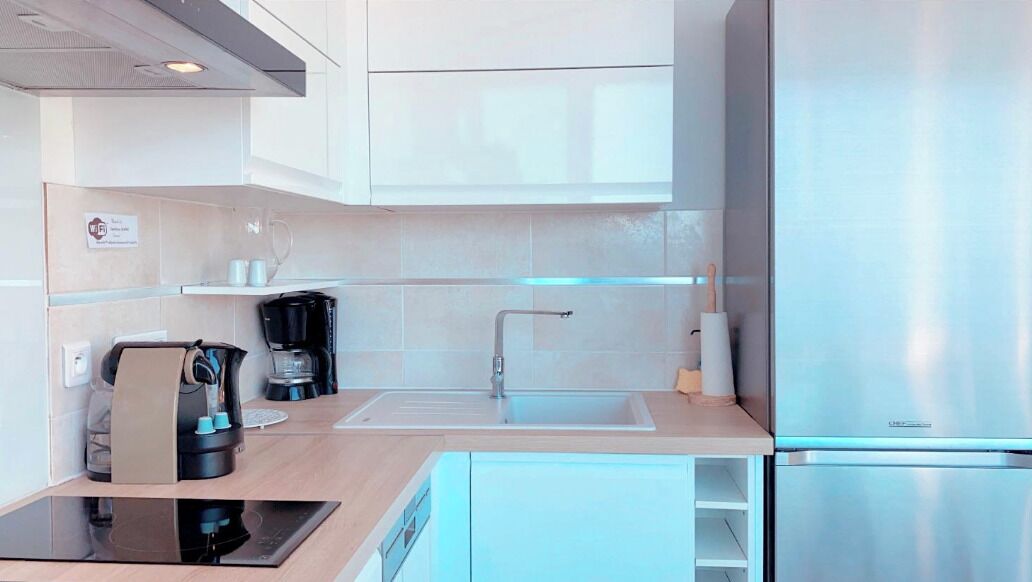 A modern kitchen with a stainless steel refrigerator, a coffee machine, and a sink.
