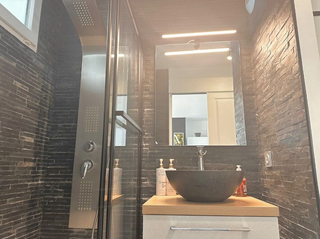 Une salle de bain moderne avec un grand lavabo noir sur pied, une douche en verre et un miroir au-dessus du lavabo.