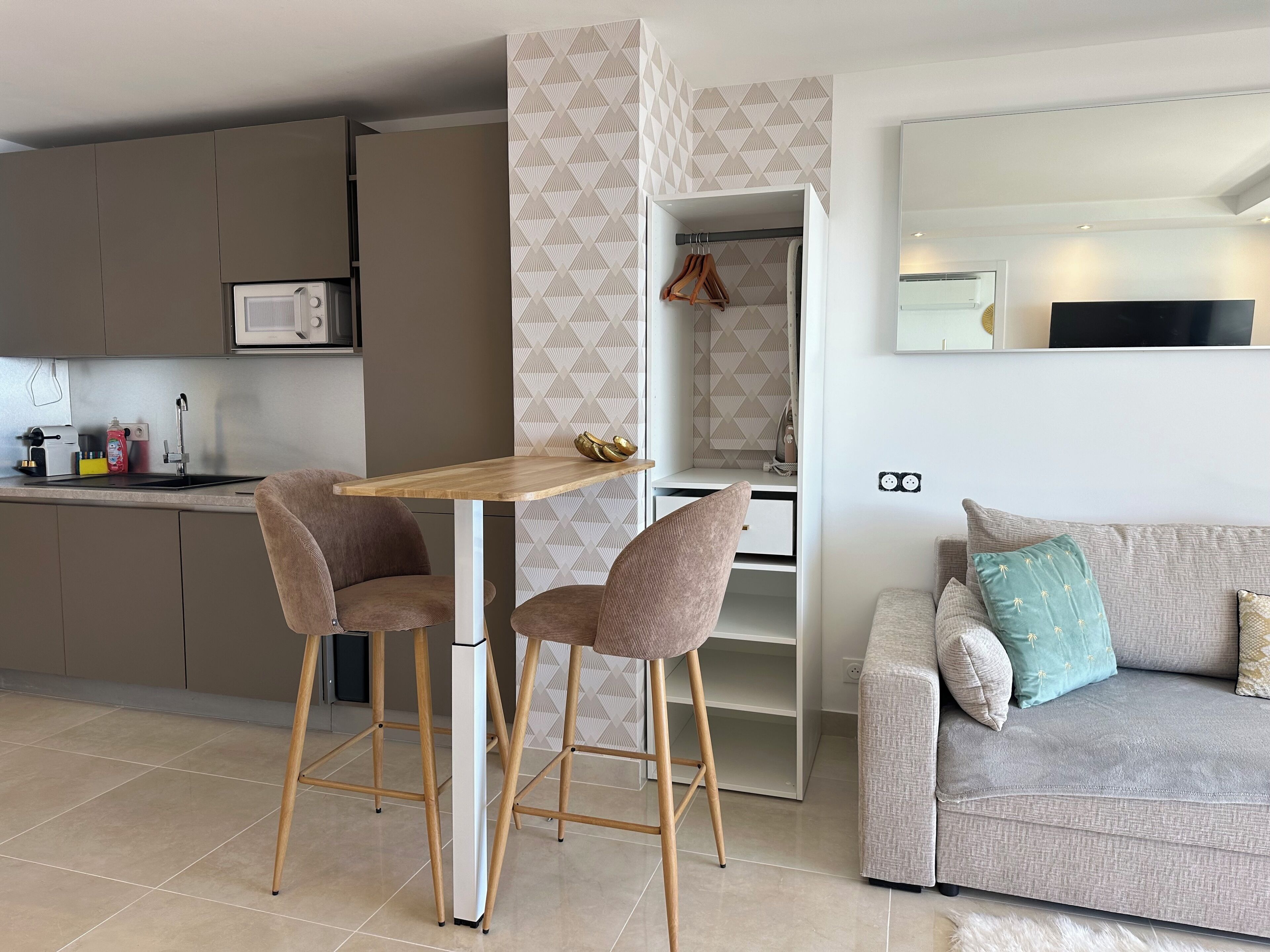 A modern kitchen with a microwave, sink, and bar stools. There is a dining table with chairs, a sofa, and a TV.