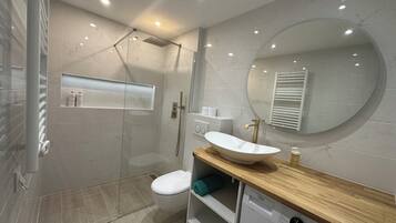 Ein modernes Badezimmer mit einer Duschkabine, einem weißen Waschbecken und einer integrierten Waschmaschine.