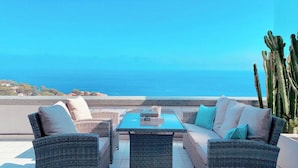 Une terrasse dotée de meubles en osier, d’une table et offrant une vue sur la mer.