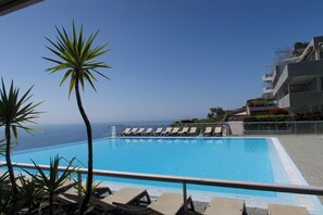 A clear blue pool with lounge chairs, palm trees, and a view of the ocean.