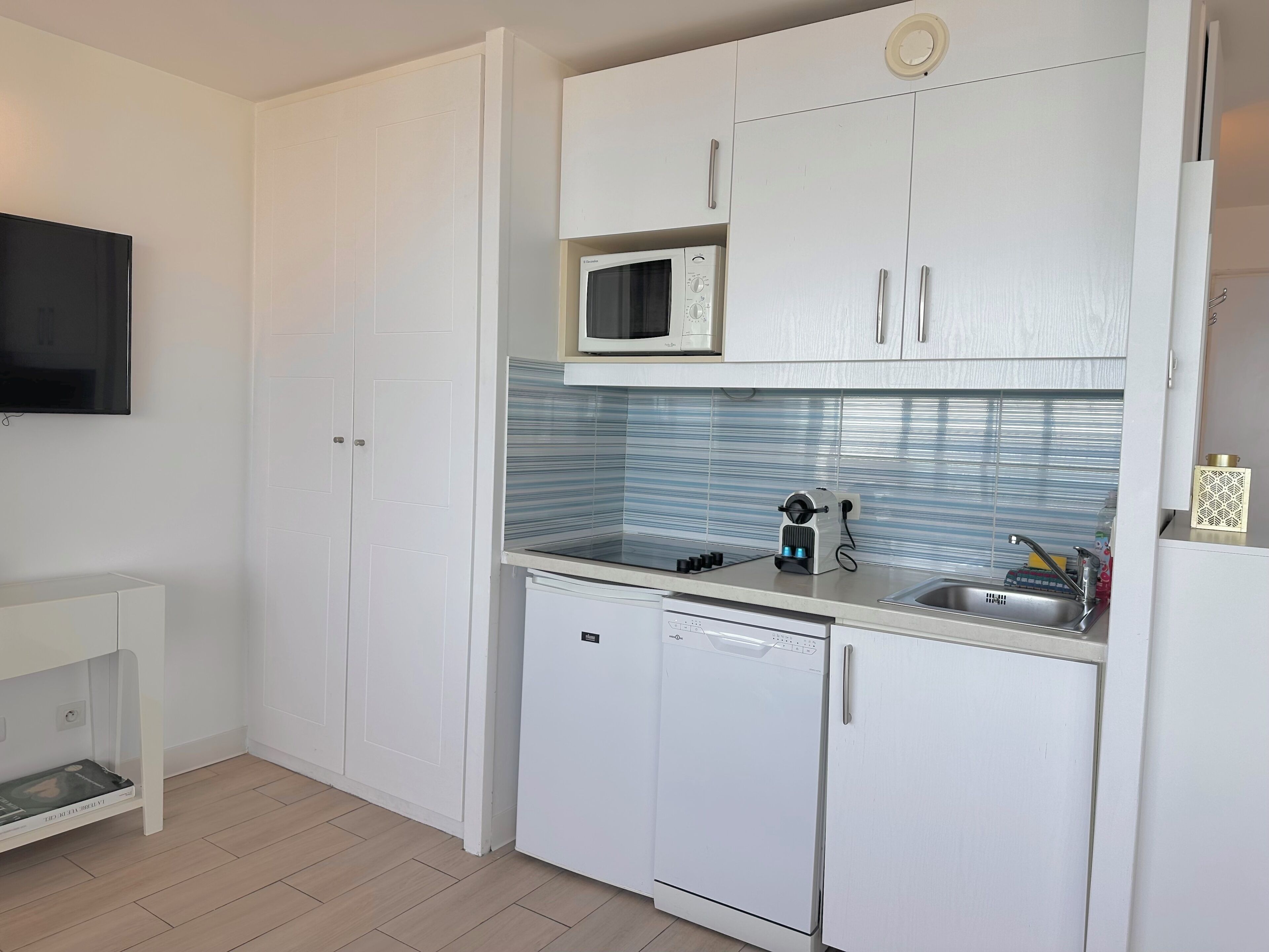 Pieni, käytännöllinen keittiö, jossa on valkoiset kaapit, mikroaaltouuni, pesuallas ja astianpesukone.