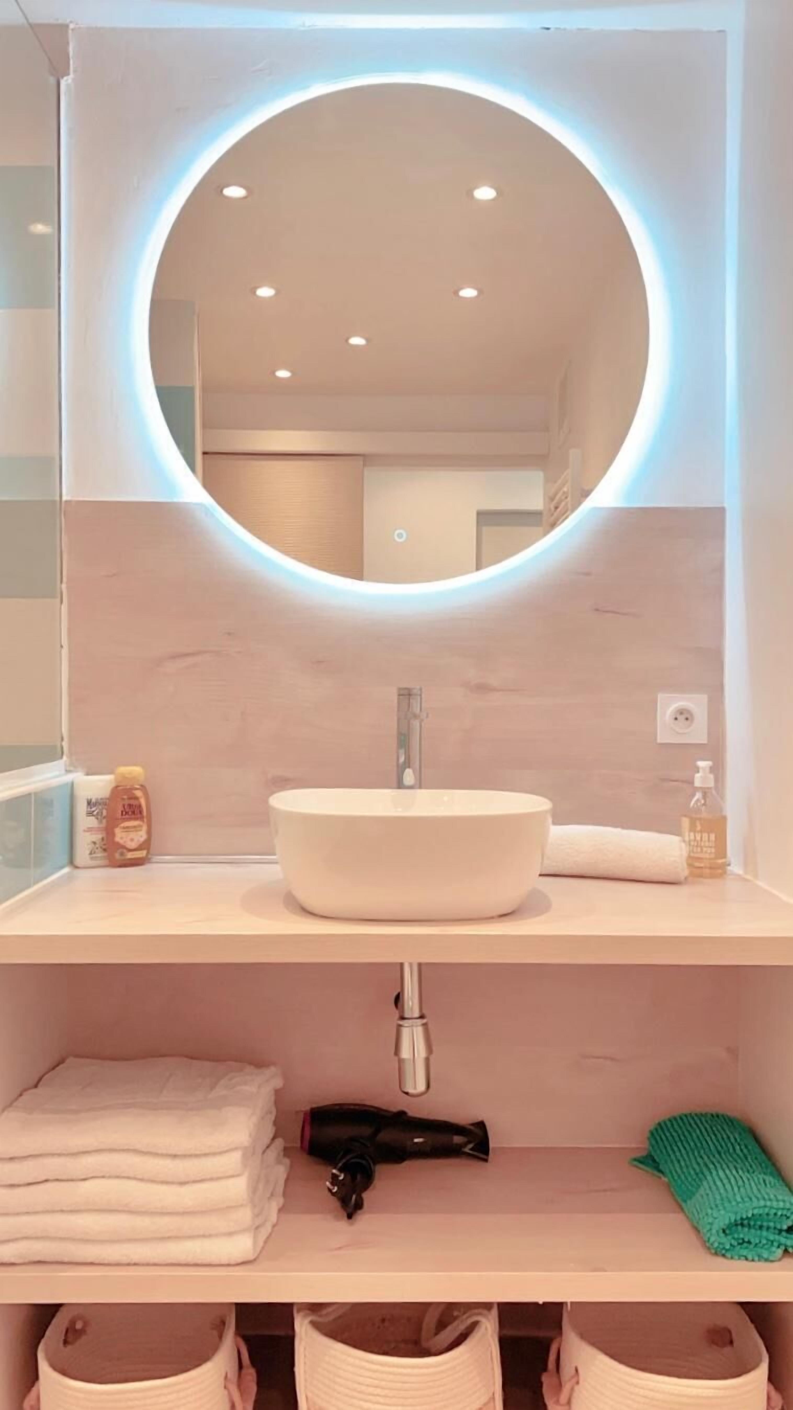 Uma casa de banho moderna com um espelho redondo, uma pia e uma prateleira com toalhas e produtos de higiene pessoal.