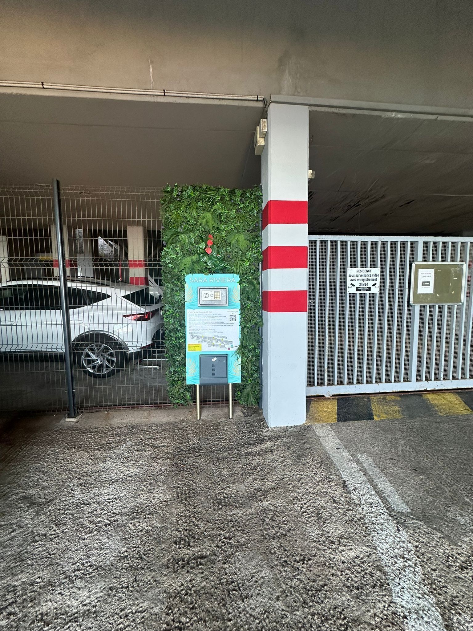 Un aparcament amb un cotxe blanc a dins, una càmera de seguretat i un senyal que indica vigilància.