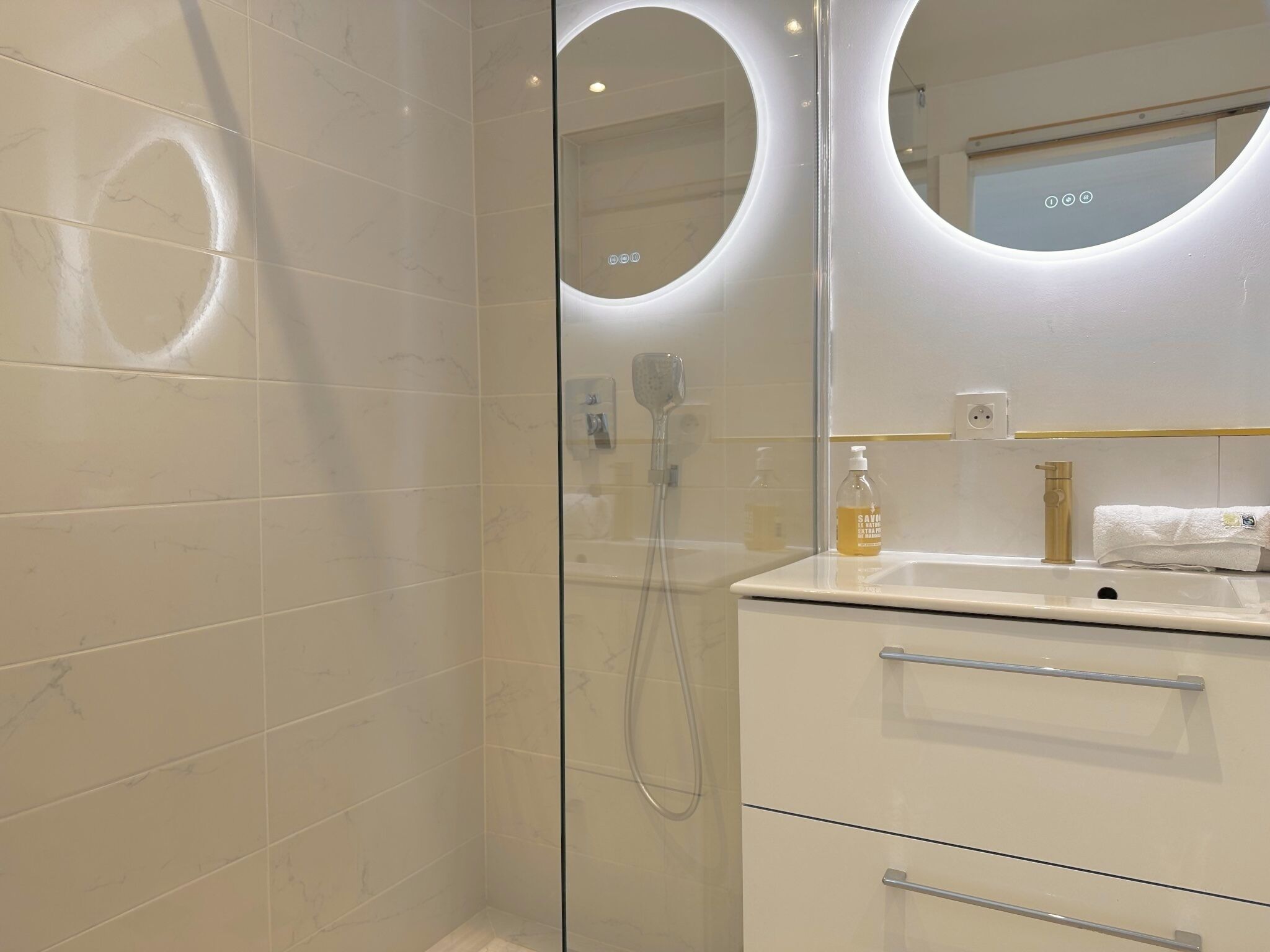 A modern bathroom with a glass-enclosed shower, a white vanity with a mirror, and a towel rack.