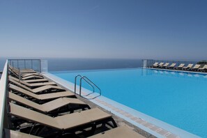 A pool with lounge chairs and a view of the ocean.