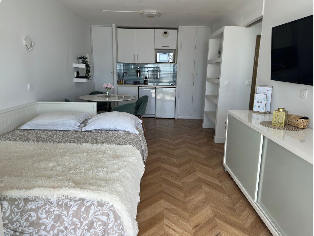 Quarto de hotel compacto com uma cama, uma pequena cozinha e uma televisão.
