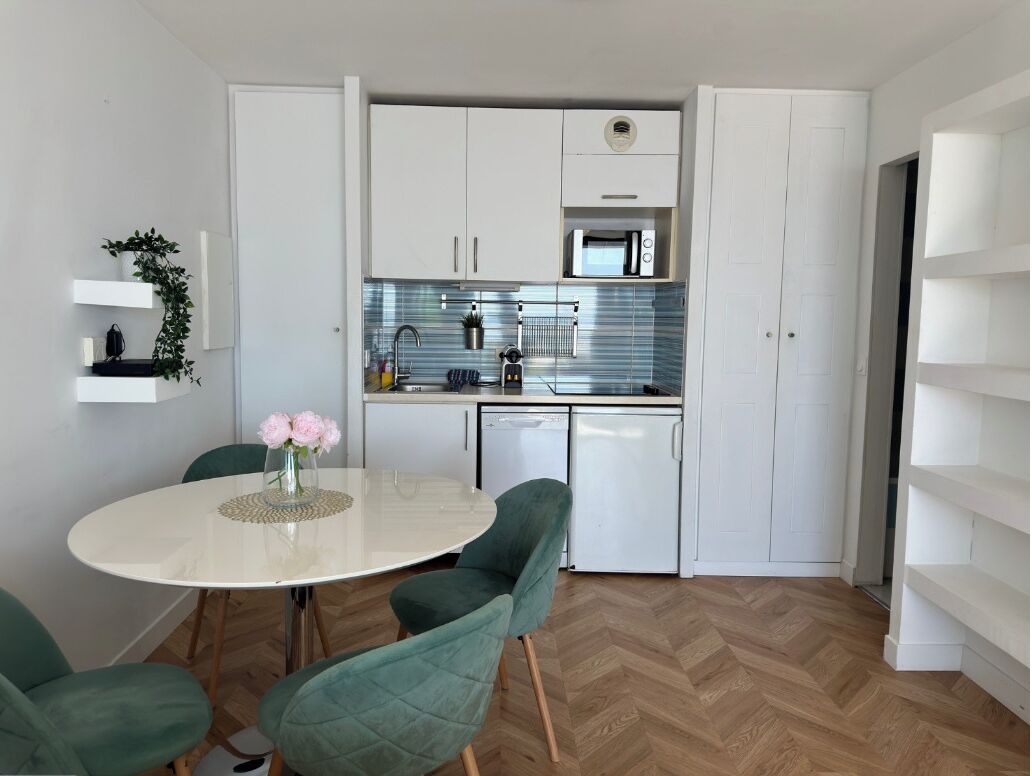 A compact kitchen with white cabinets, a microwave, and a sink. There is a dining table with chairs and a vase of flowers.