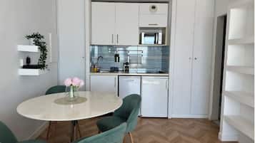 A compact kitchen with white cabinets, a microwave, and a sink. There is a dining table with chairs and a vase of flowers.