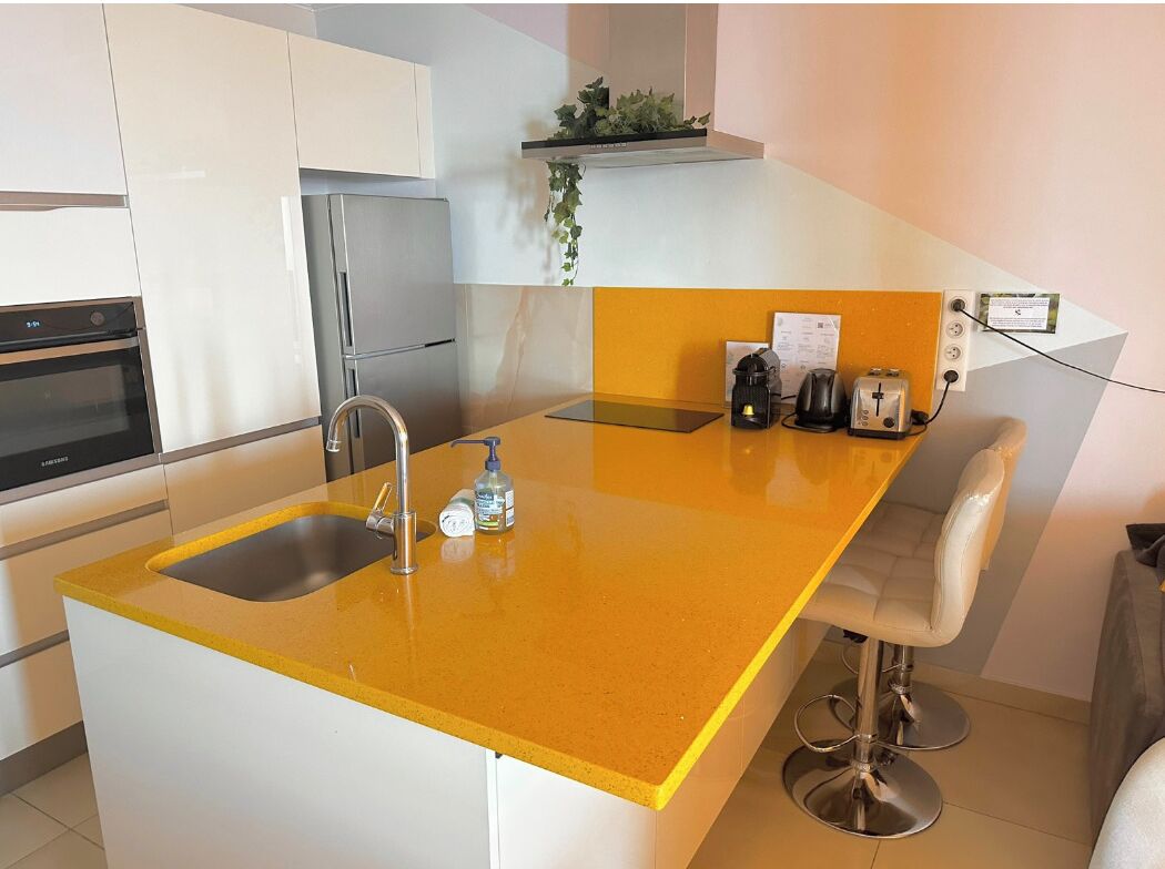 A modern kitchen with a yellow countertop, stainless steel appliances, and a bar stool.