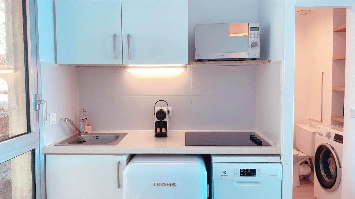 A compact kitchen with a sink, a microwave, a coffee machine, and a dishwasher.