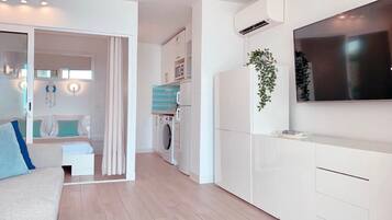 Un appartement moderne comprenant un espace de vie, une cuisine équipée d’un lave-linge et d’un sèche-linge intégrés, et un grand téléviseur fixé au mur.