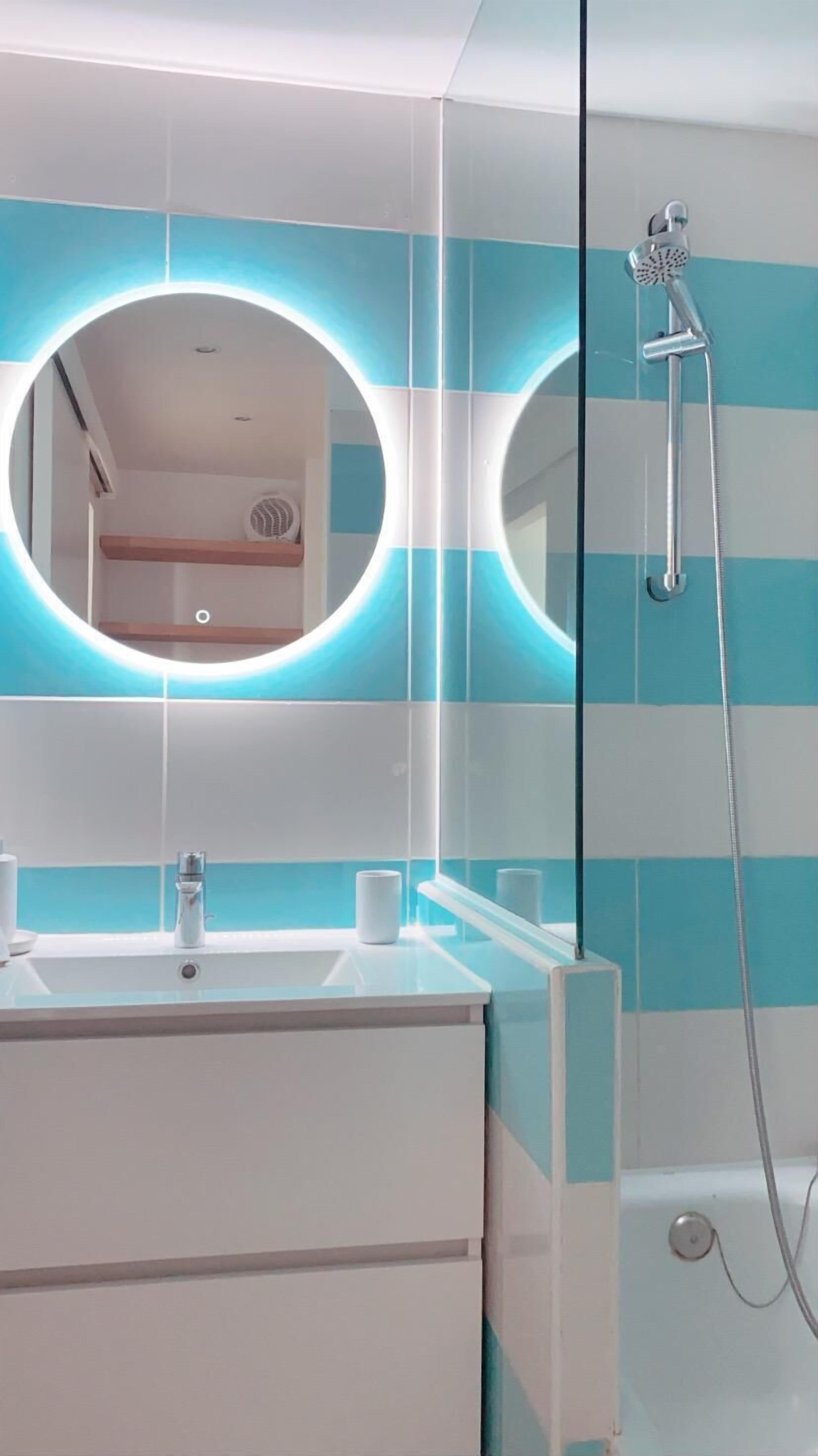 A bathroom with a modern design, featuring a round mirror, a sink, and a shower.