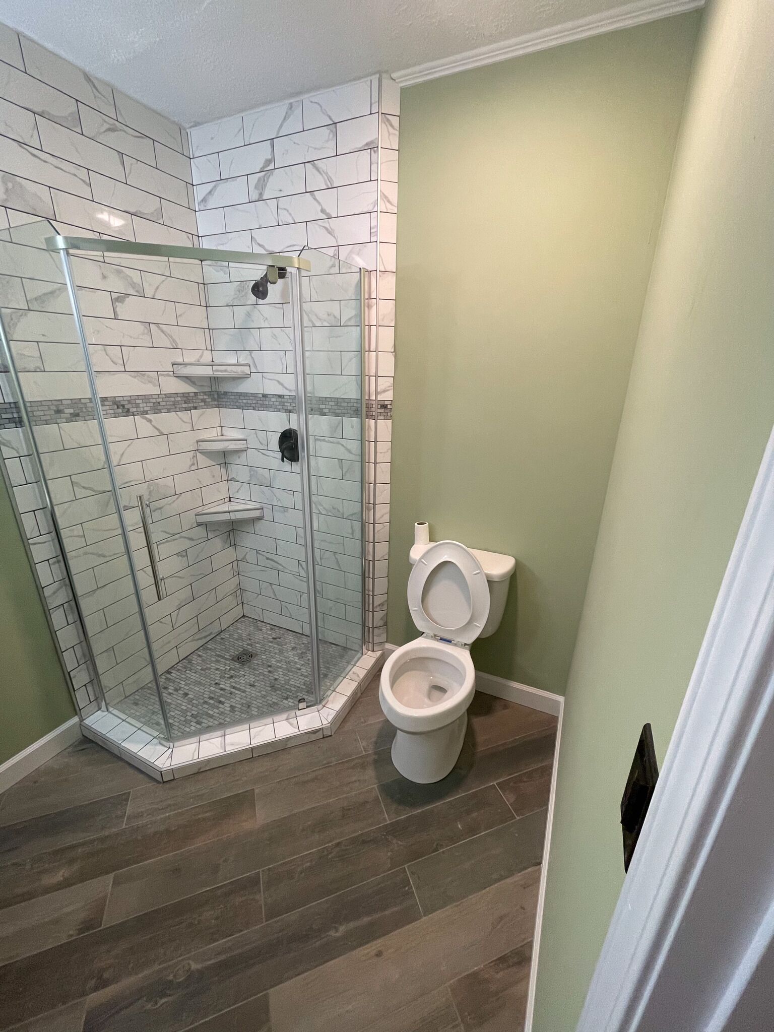Un baño con ducha de vidrio, inodoro y pared con estampado de mármol.