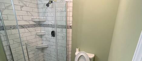 Un baño con ducha de vidrio, inodoro y pared con estampado de mármol.
