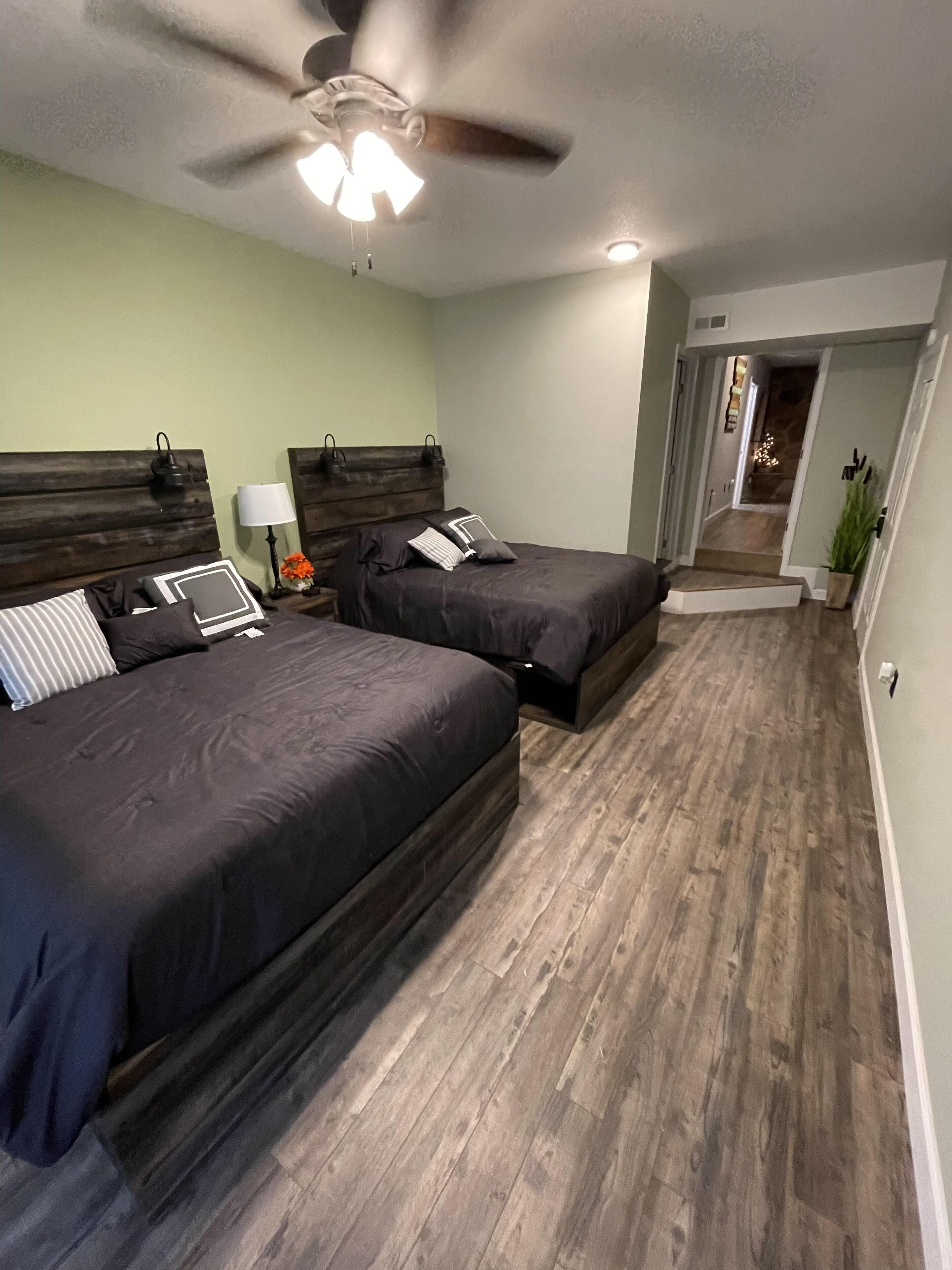 A bedroom with two beds, a ceiling fan, and a nightstand with a lamp.