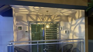 Een balkon met twee rieten stoelen, een glazen balustrade en een decoratieve verlichtingsarmatuur.
