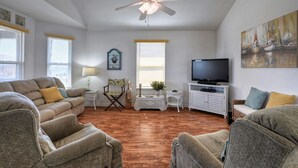 A spacious living room with a ceiling fan, a television, and a painting on the wall. - Beautiful island paradise only 6 blocks to the beach (Galveston)