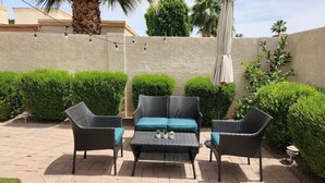 Een terras buiten met rieten meubels, een tafel en een decoratieve parasol.