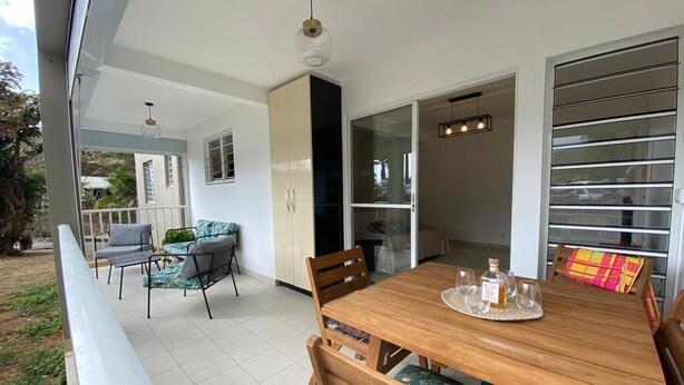 Un coin repas avec une table et des chaises en bois, une porte vitrée donnant sur un balcon et un luminaire au plafond.
