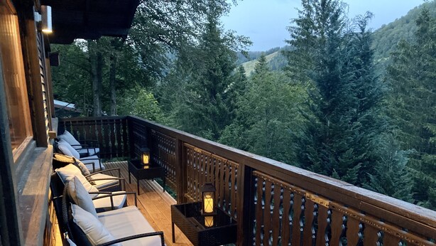 Une terrasse en bois avec des sièges d’extérieur et des lanternes, offrant une vue sur une colline boisée.
