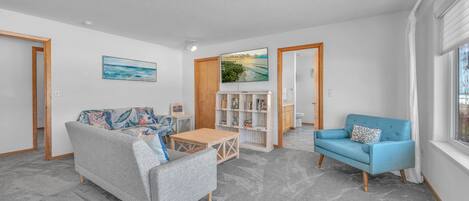 Una sala de estar con un sofá gris, un sillón azul, una mesa de centro de madera y una estantería.