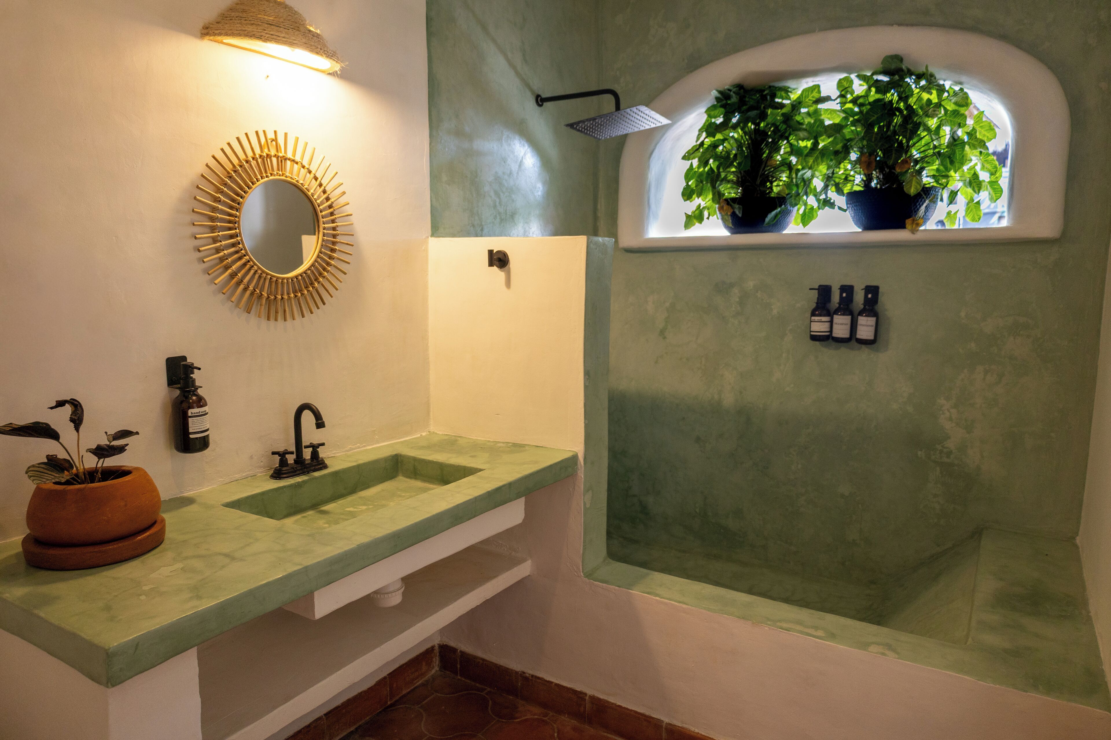 A bathroom with a green sink, a mirror, a shower, and a window with plants.