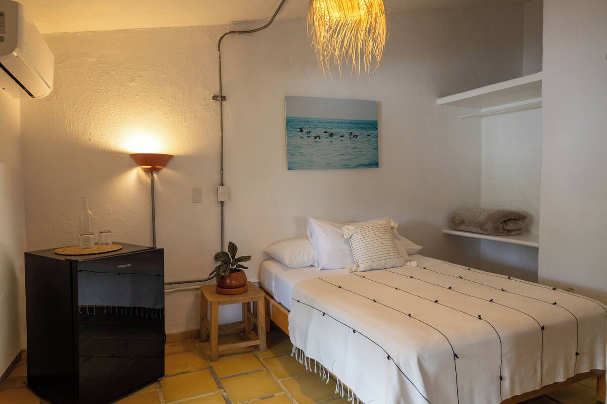 A bedroom with a bed, a bedside table with a plant, a wall-mounted shelf, and a painting of birds on the wall.