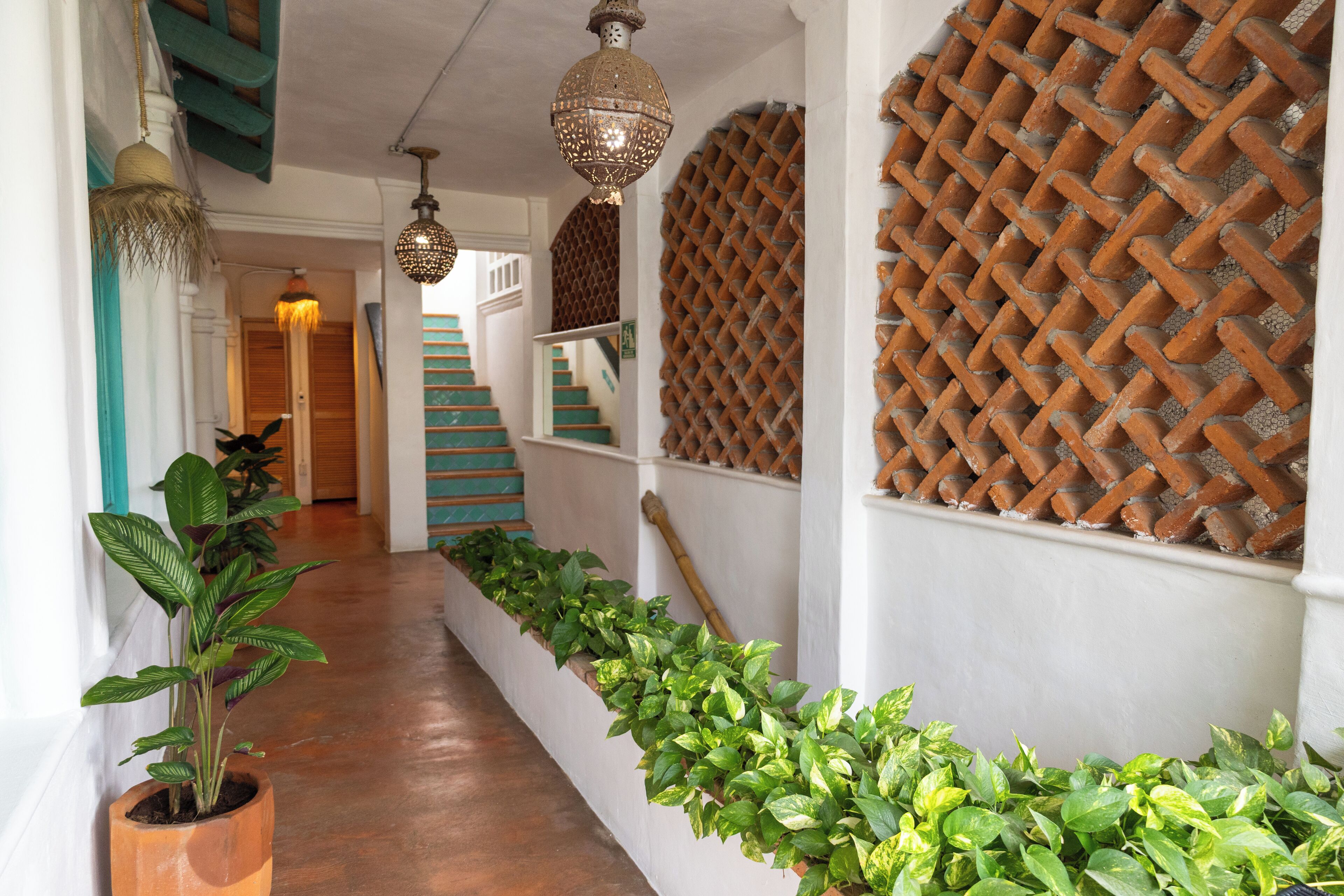 Un pasillo con suelo de madera, plantas verdes y una escalera con diseño de celosía.