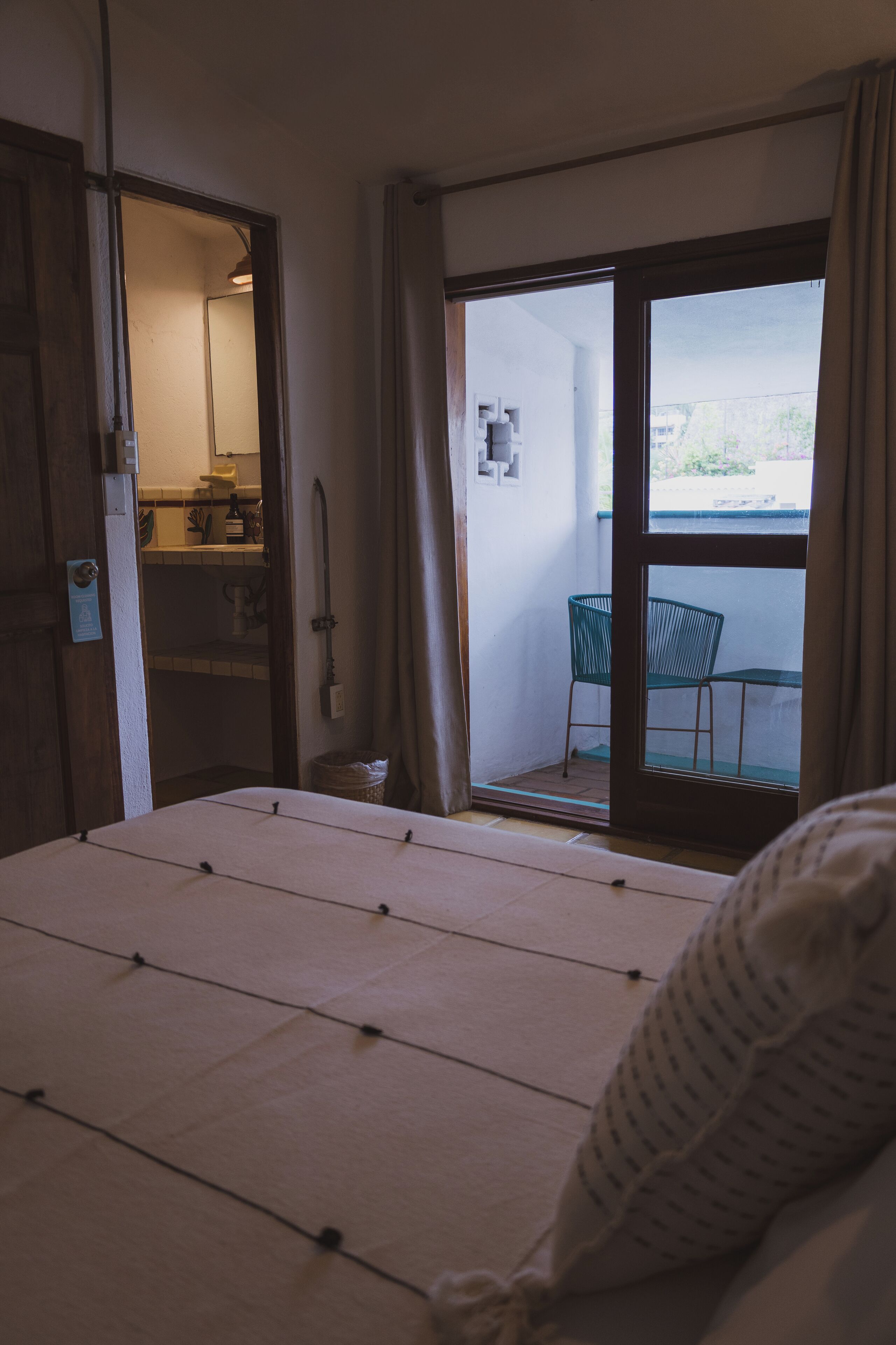 Une chambre avec un lit, une salle de bain visible à travers une porte ouverte et un balcon avec une chaise.