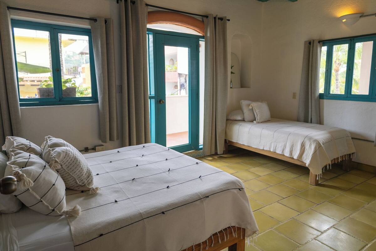A bedroom with a large bed, a smaller bed, and a window with curtains.