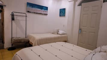 Un dormitorio con cama, una mesita de noche pequeña, un perchero en la pared y una puerta.