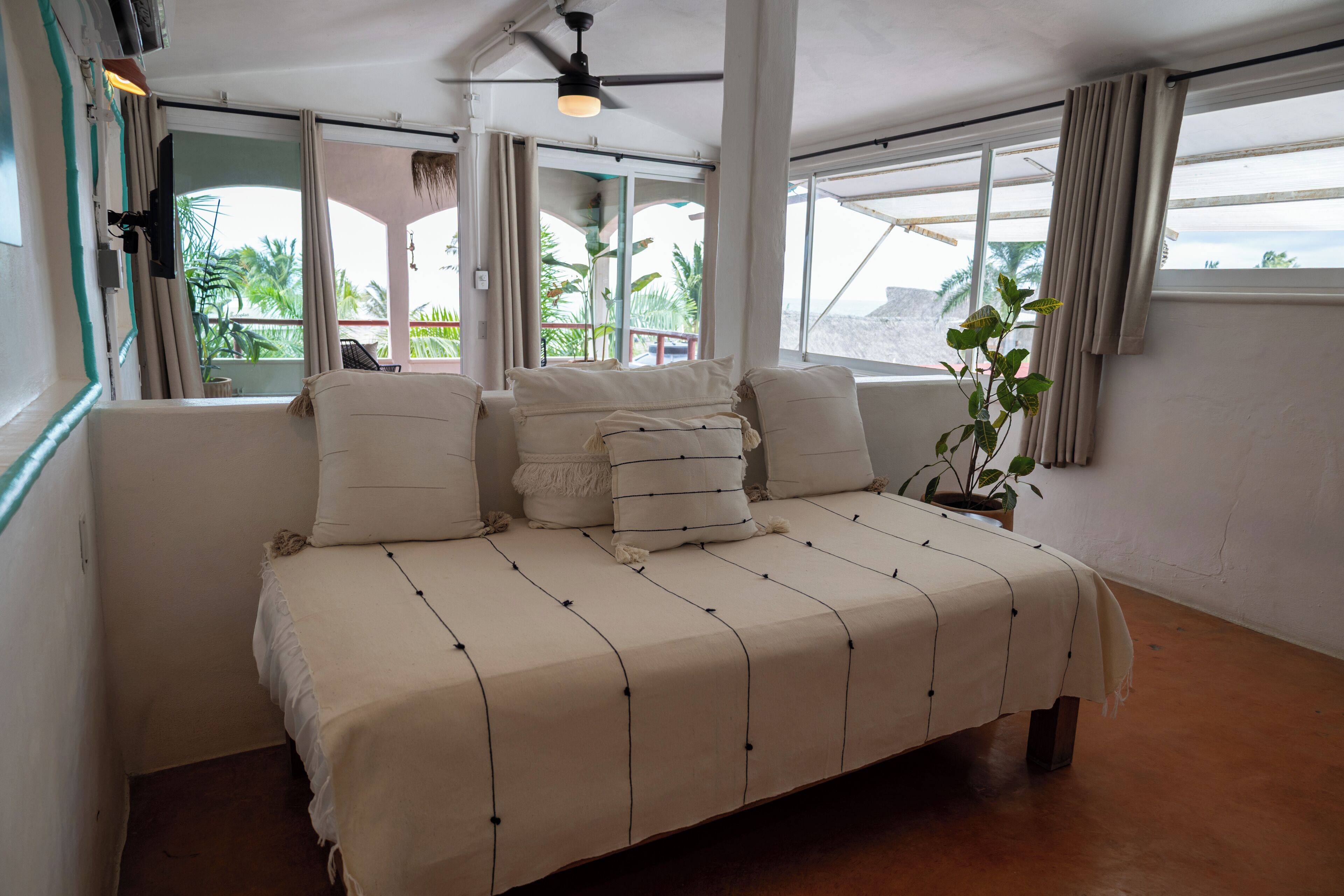 A bedroom with a large bed, a ceiling fan, and a view of the outdoors.
