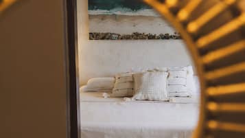 Una cama con ropa de cama blanca y una almohada estampada, una pared con un cuadro y un espejo con un marco de rayos de sol.