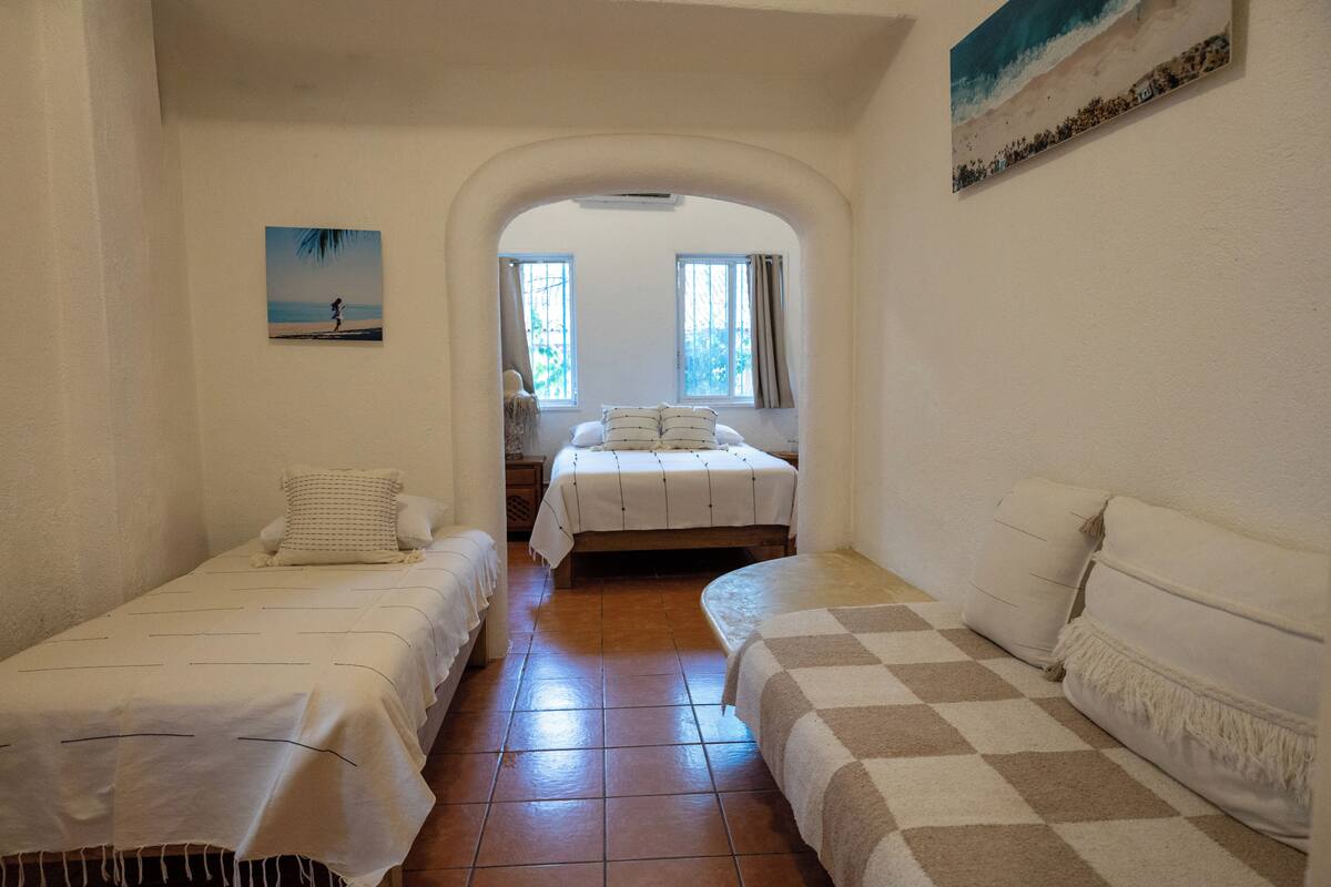 A room with two beds, a large window, and a painting on the wall.
