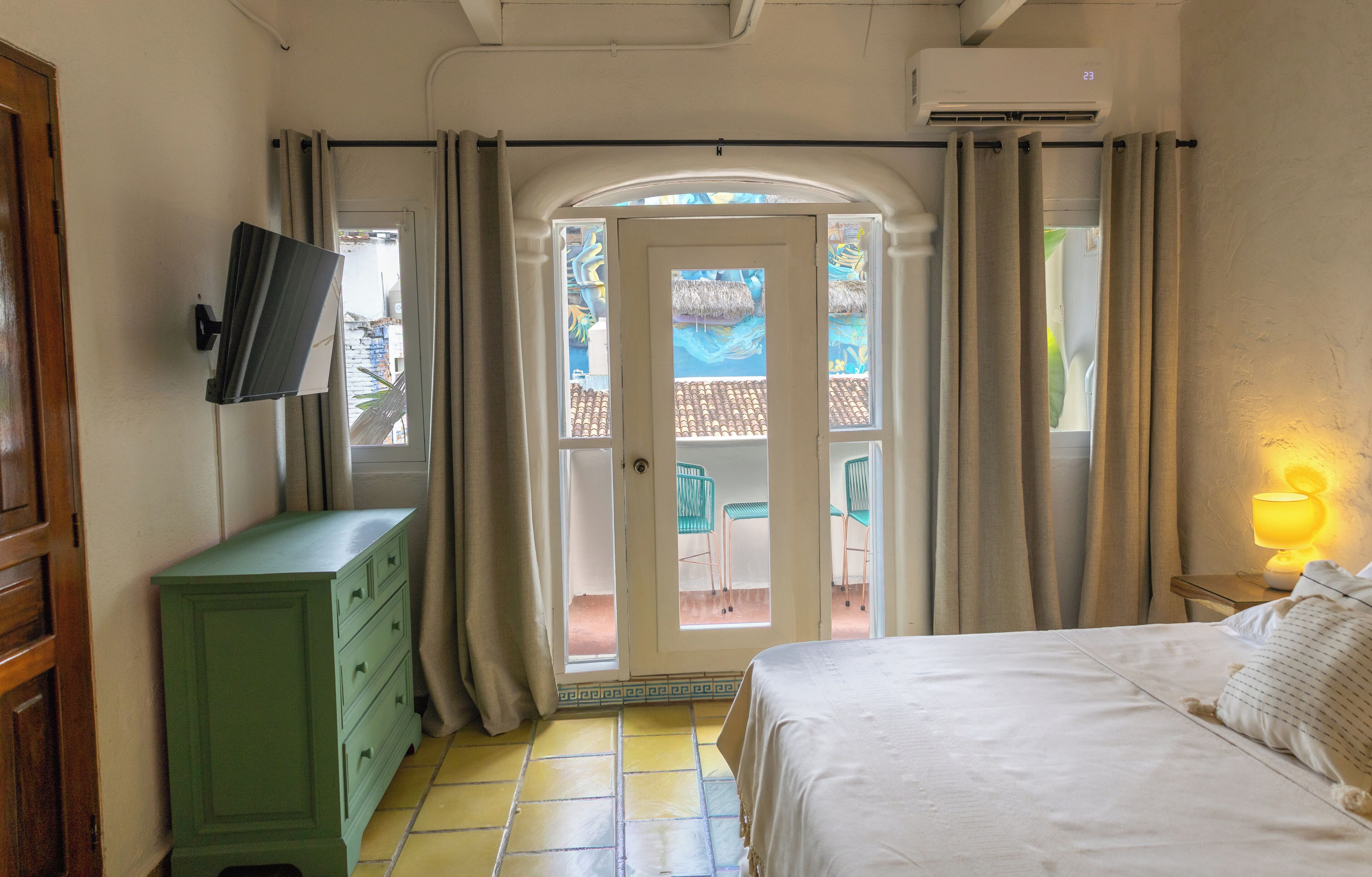Une chambre d’hôtel avec un lit, une commode, un téléviseur fixé au mur et un balcon équipé de chaises.