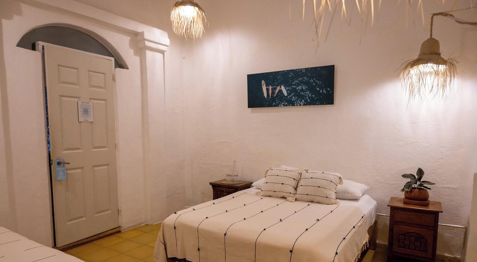 Une chambre à coucher avec un lit, une table de chevet, une plante en pot, un tableau et une porte avec une pancarte.