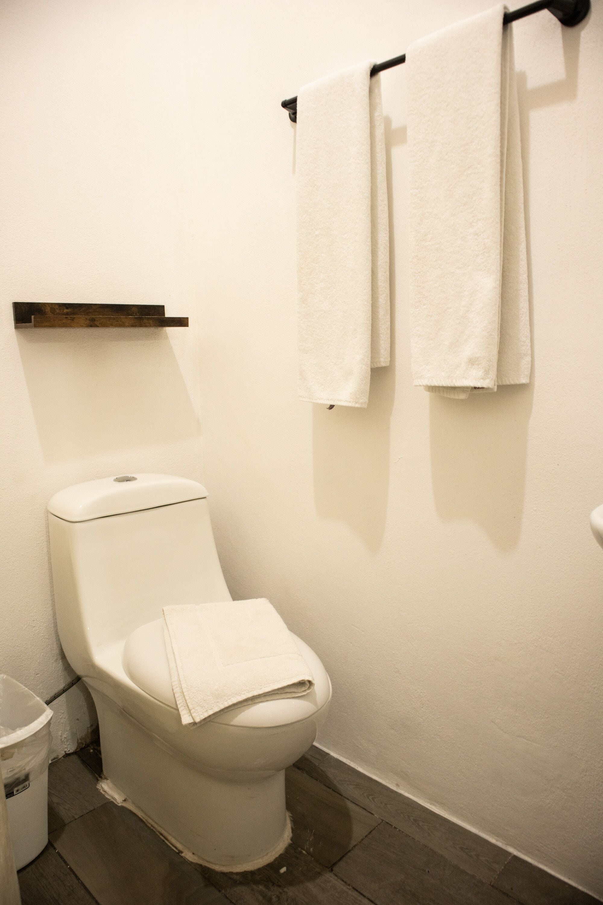 Een schone, witte badkamer met een toilet, een klein plankje erboven en twee handdoeken aan een rek.