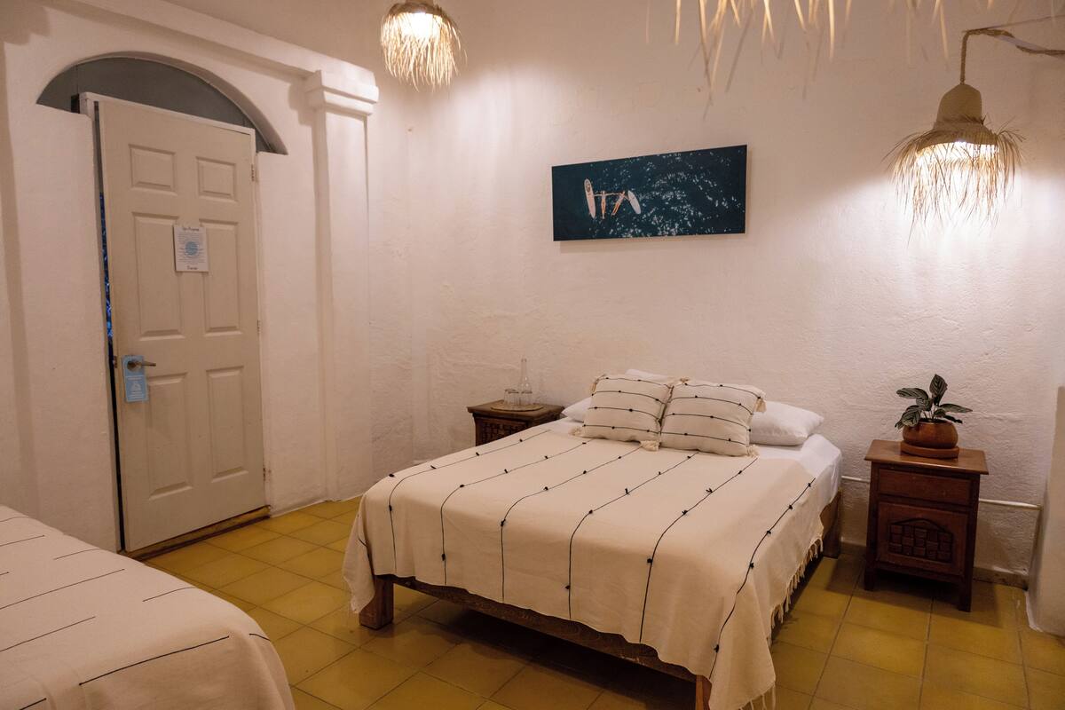 A bedroom with a bed, a nightstand, a potted plant, a door, and a wall-mounted painting.