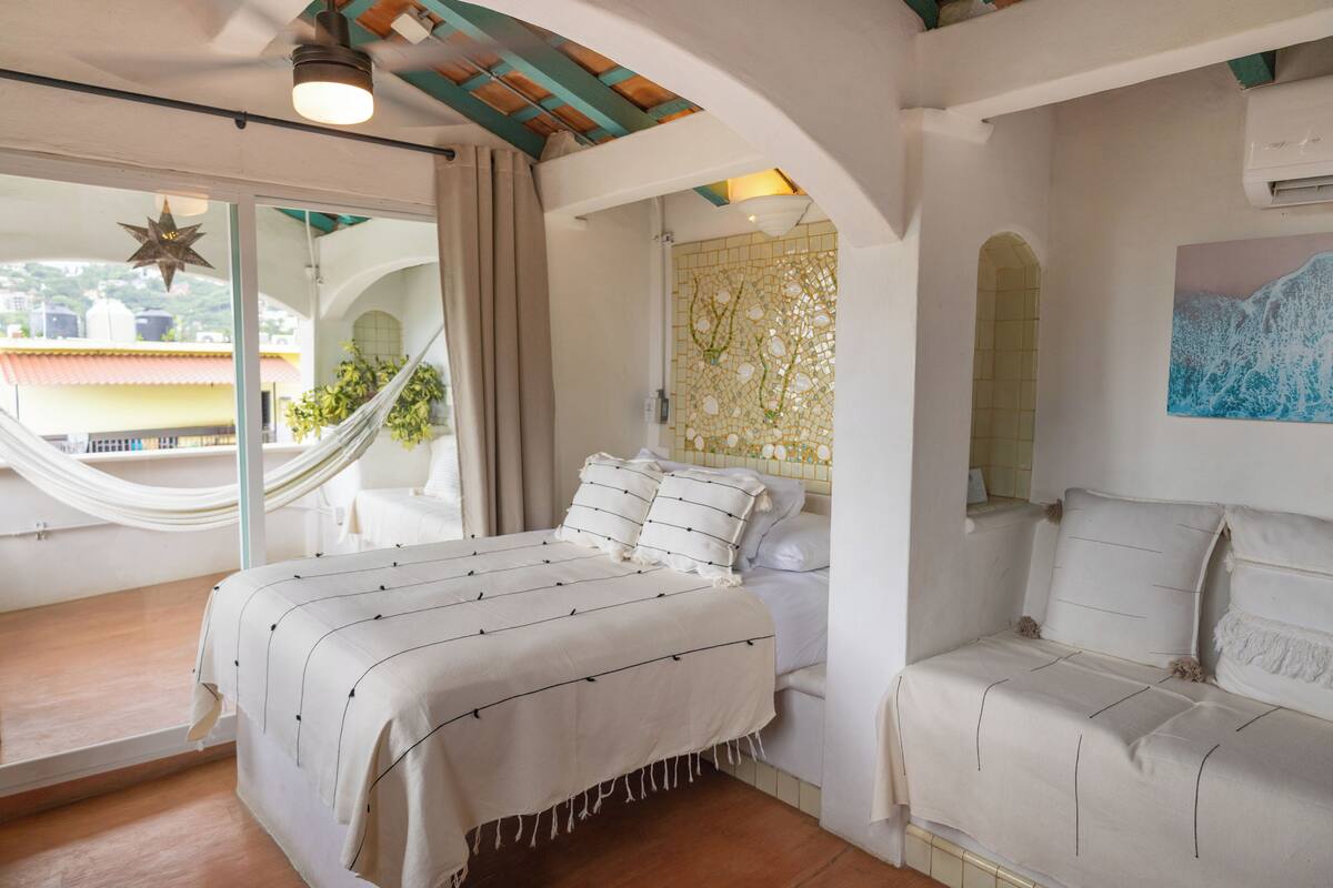 A bedroom with a bed, a hammock, and a view of the outside.