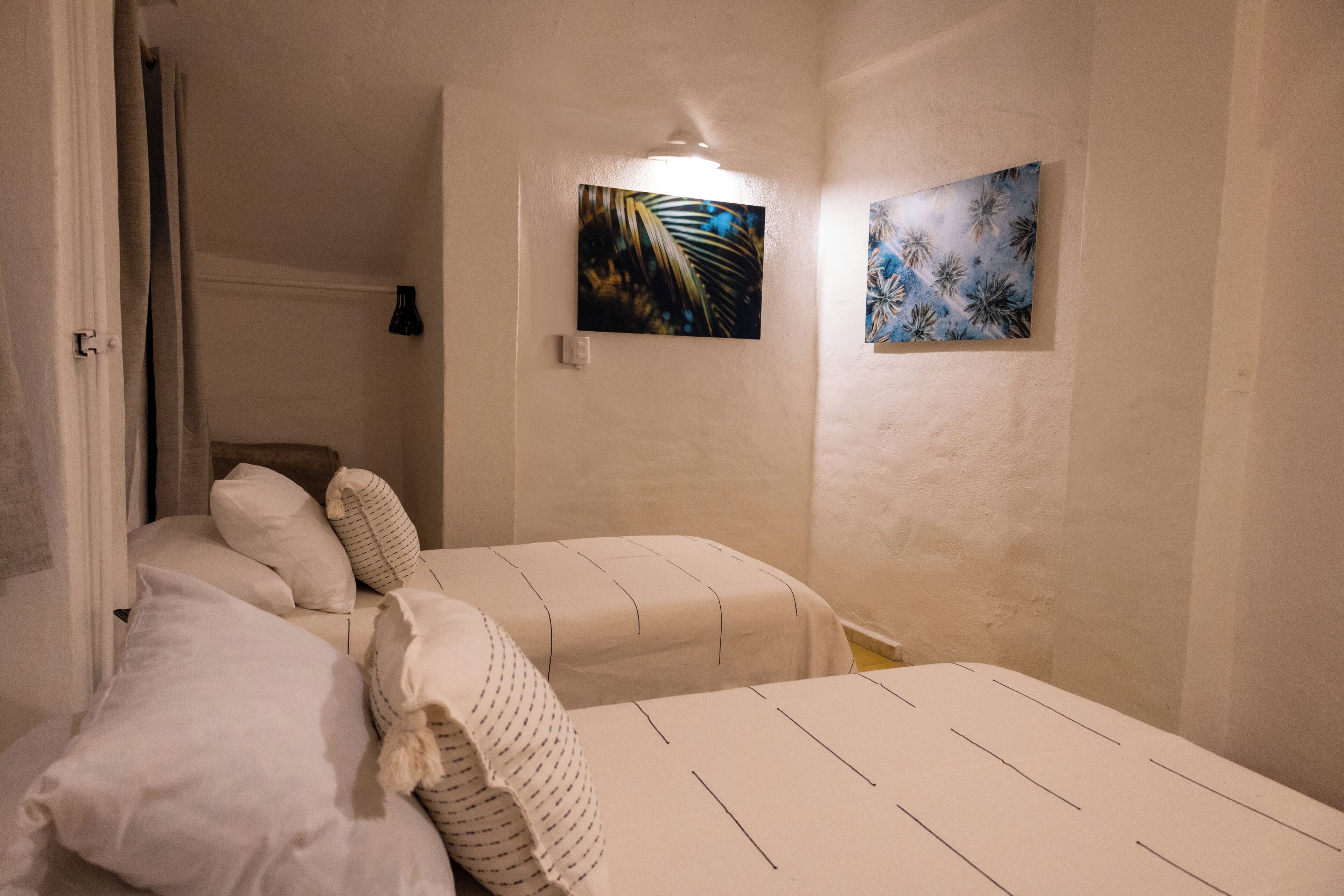 Une chambre avec deux lits, une table de chevet et deux tableaux accrochés au mur.